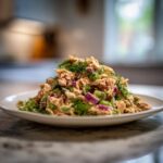 A mound of fresh salmon salad mixed with red onion and celery, topped with dill, ready to eat.