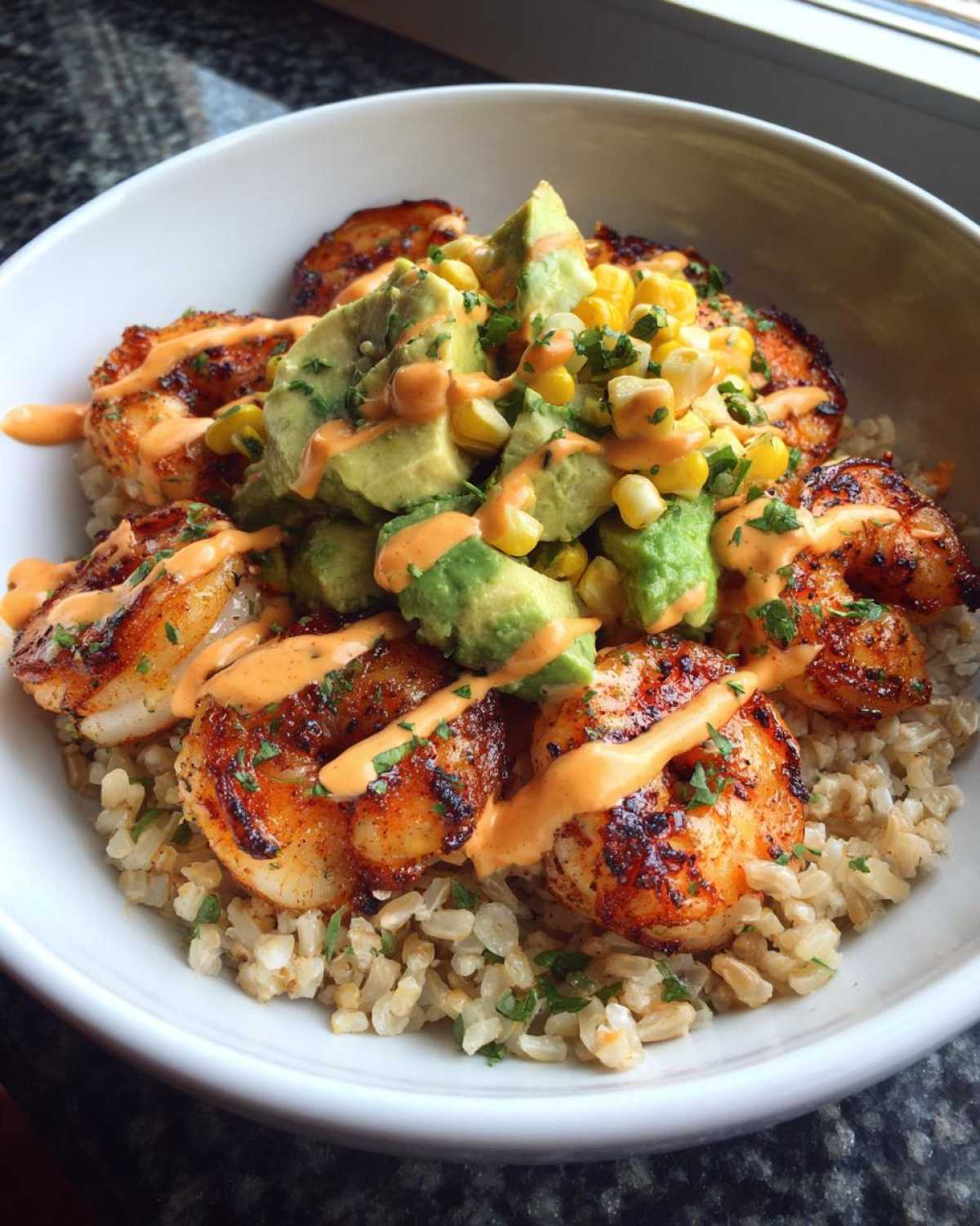 Close-up of a delicious shrimp bowl featuring seasoned shrimp, brown rice, avocado, corn, and a creamy sauce.