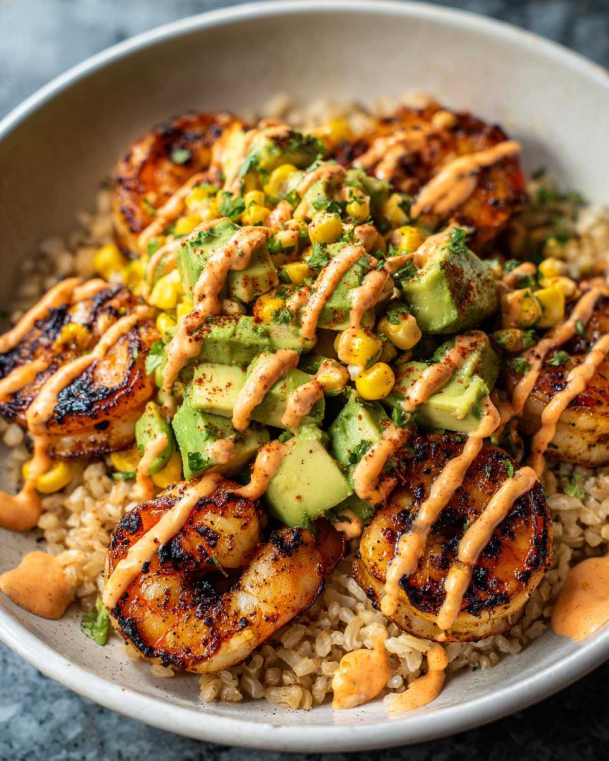 Close-up of an amazing shrimp bowl featuring grilled shrimp, avocado, corn salsa, and spicy sauce over brown rice.