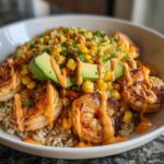 Close-up of an amazing shrimp bowl featuring grilled shrimp, brown rice, corn salsa, avocado slices, and spicy orange sauce.