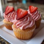Three perfectly baked strawberry cupcakes topped with swirls of pink frosting and a fresh strawberry slice.