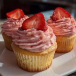 Three delicious strawberry cupcakes topped with pink frosting and fresh strawberry slices, ready to eat.