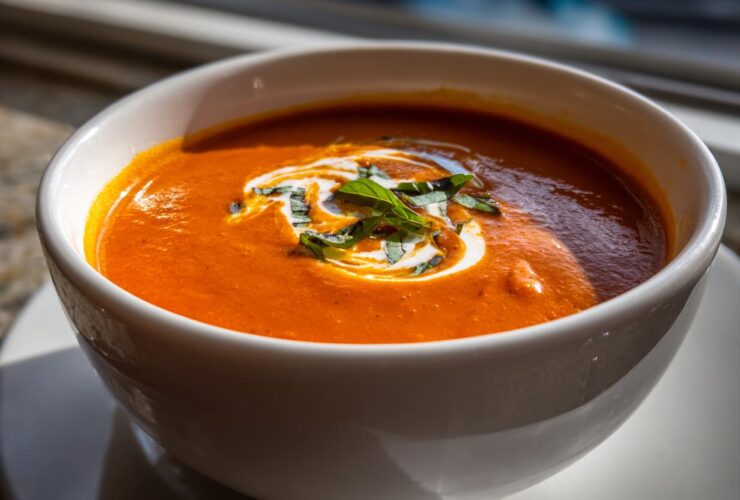 Close-up of a vibrant orange tomato bisque in a white bowl, garnished with a swirl of cream and fresh basil.