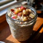 Close-up of a glass jar filled with creamy apple cinnamon overnight oats, topped with fresh diced apples and a sprinkle of cinnamon.