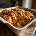 Close-up of a freshly baked apple crisp recipe showing warm, bubbly apples under a golden, crunchy oat topping.