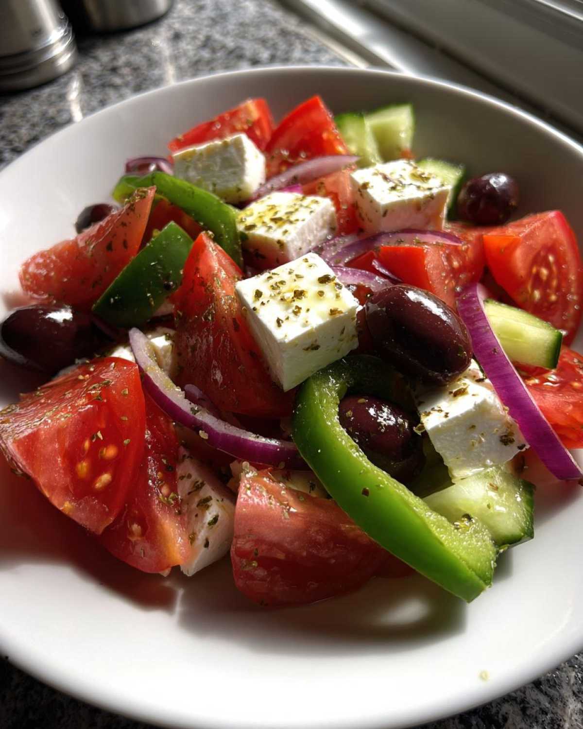 A vibrant bowl of authentic greek salad featuring large chunks of tomato, cucumber, green pepper, red onion, Kalamata olives, and feta cheese.