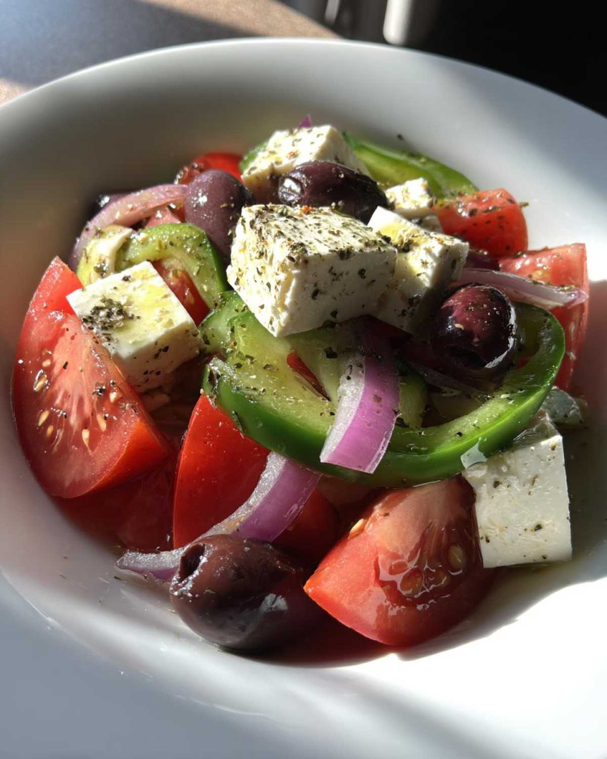 Close-up of a vibrant greek salad featuring large chunks of feta cheese, ripe tomatoes, green peppers, red onion, and Kalamata olives.