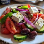 Close-up of an authentic greek salad featuring large cubes of feta, tomatoes, cucumbers, red onion, and Kalamata olives.