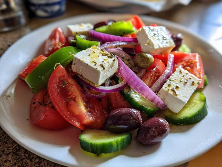 Close-up of an authentic greek salad featuring large cubes of feta, tomatoes, cucumbers, red onion, and Kalamata olives.