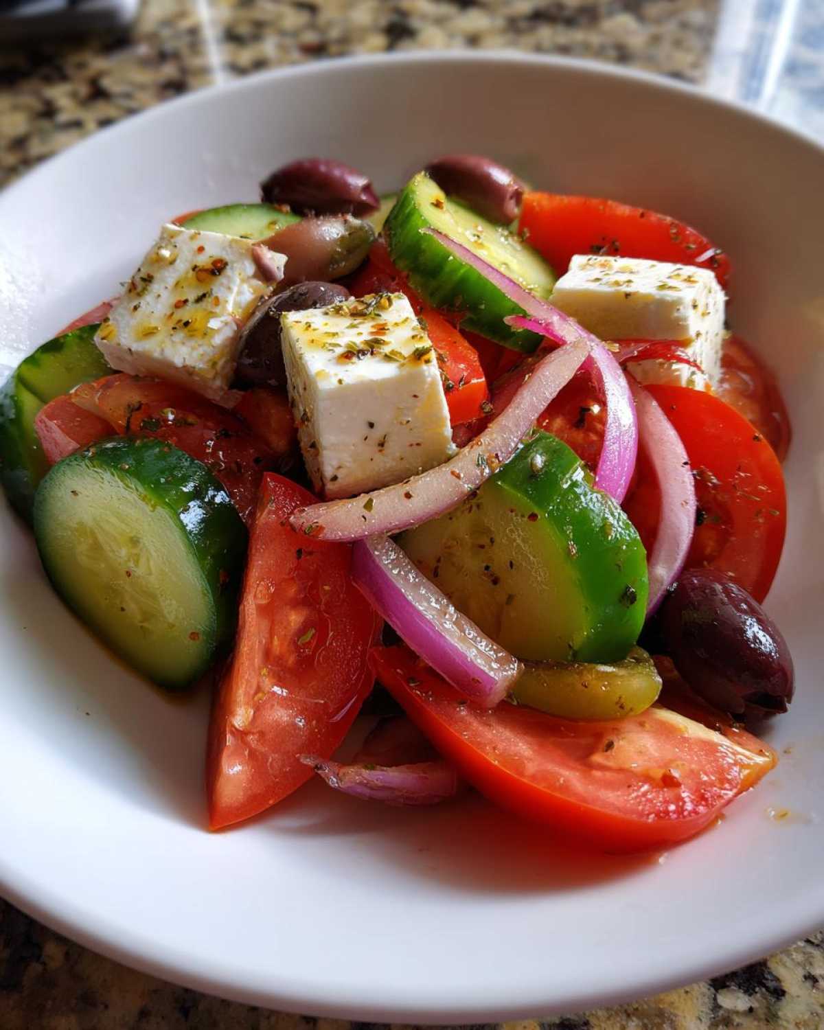 Close-up of a vibrant greek salad featuring large chunks of feta cheese, tomatoes, cucumbers, red onion, and Kalamata olives.