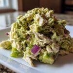 Close-up of a scoop of creamy avocado chicken salad mixed with red onion and green pepper chunks.