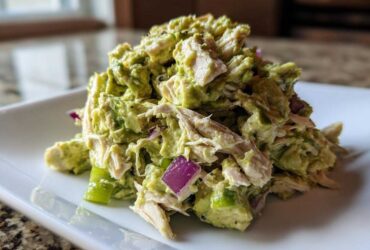 Close-up of a scoop of creamy avocado chicken salad mixed with red onion and green pepper chunks.
