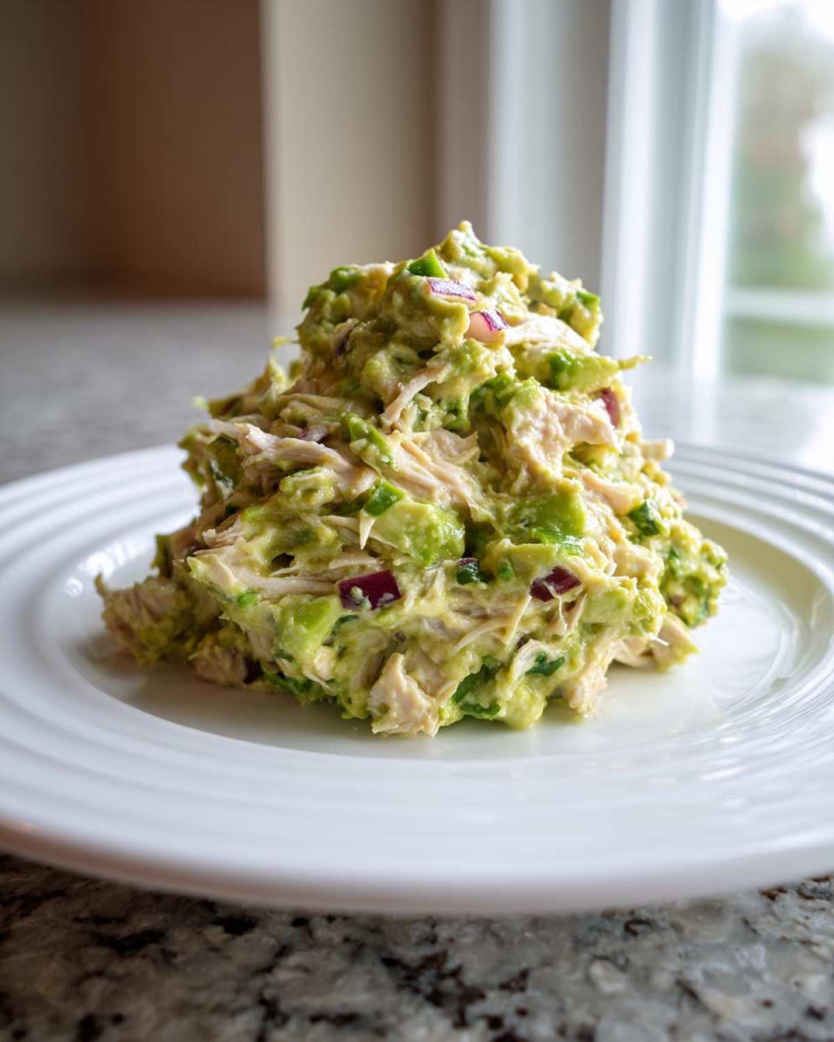 A generous serving of creamy avocado chicken salad mixed with red onion, piled high on a white plate.