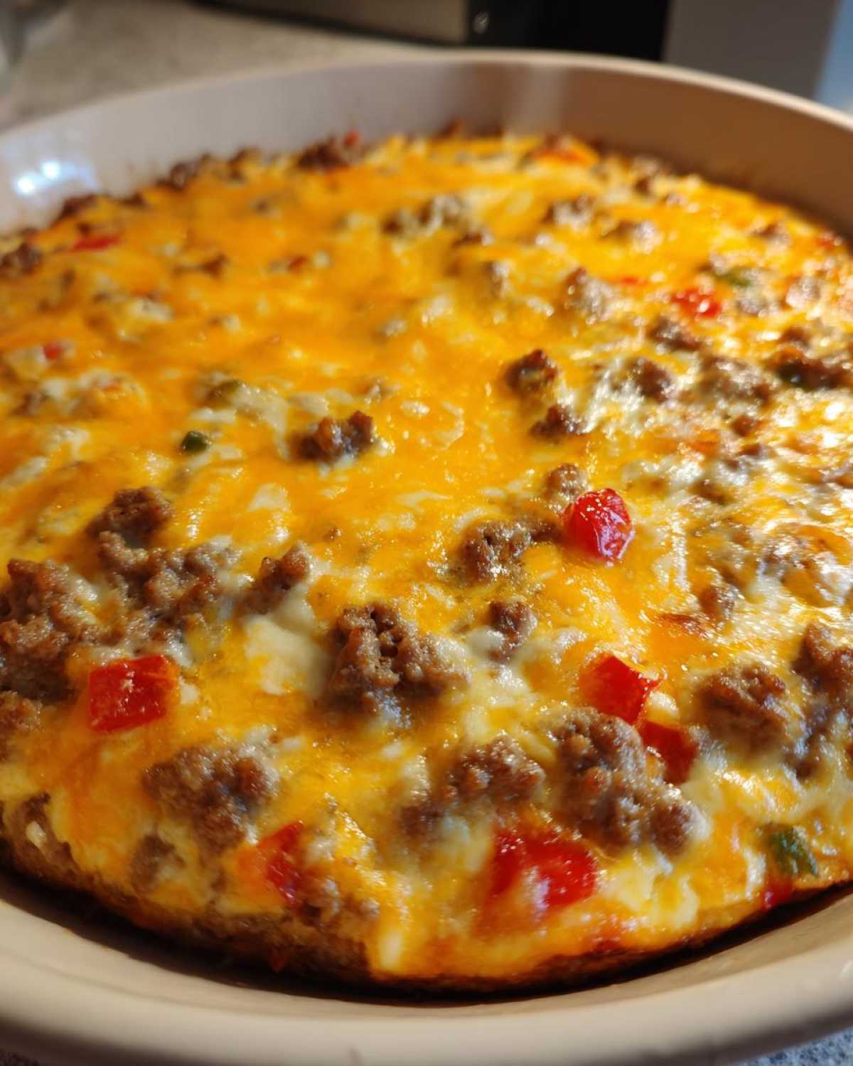 Close-up of a bubbling, baked rotel dip topped with melted cheddar cheese and ground meat.
