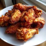 A pile of perfectly baked, crispy golden brown chicken wings served on a white plate.