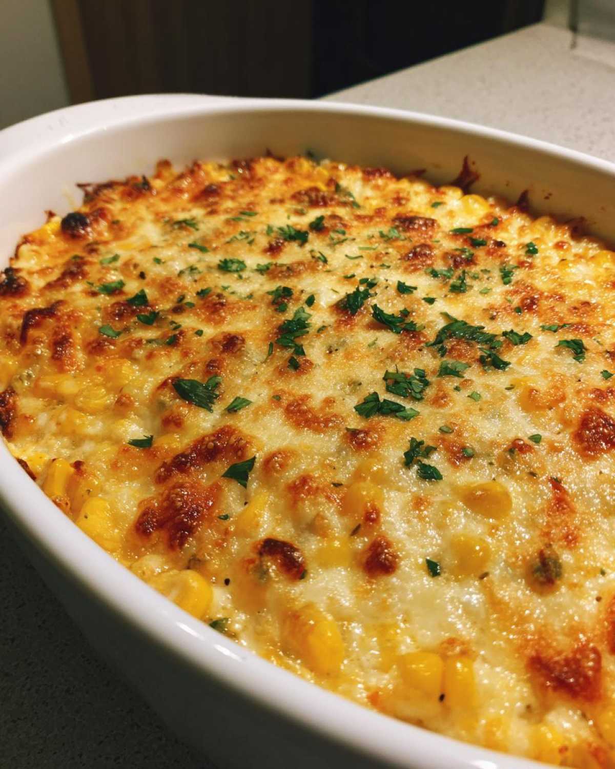 Close-up of a freshly baked elote dip with bubbly, browned cheese and fresh parsley garnish.
