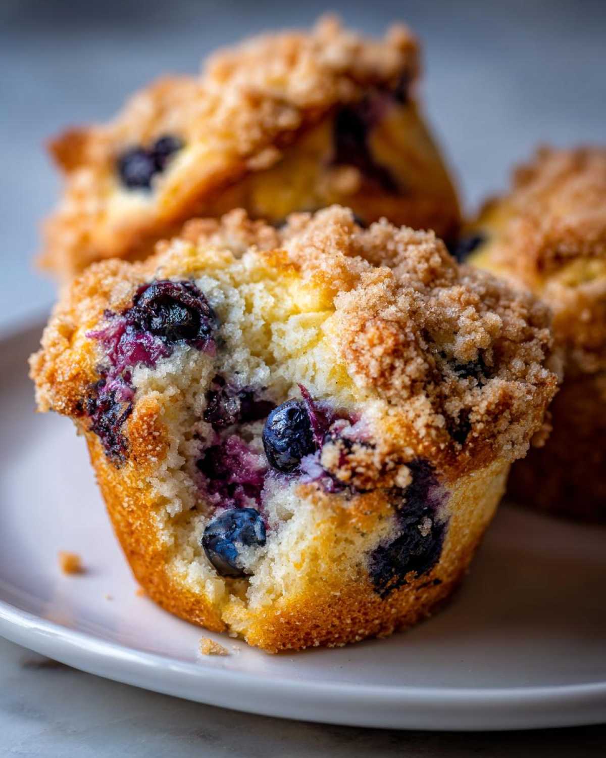 A close-up shot of a moist blueberry muffin broken open, revealing juicy berries and a thick, sugary crumb topping.