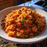 Close-up of a white bowl filled with fluffy, orange-colored spanish rice mixed with bright green peas.