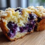 Close-up of a blueberry muffin cut in half showing moist crumb, bursting blueberries, and a crumbly streusel topping.
