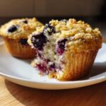 A close-up of a blueberry oatmeal muffin cut in half showing juicy blueberries, next to a whole one.