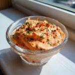 Close-up of a vibrant orange remoulade sauce topped with chopped parsley and paprika in a small glass dish.