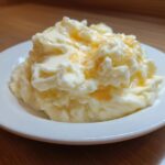 A serving of fluffy Boursin mashed potatoes topped with melted butter on a white plate.