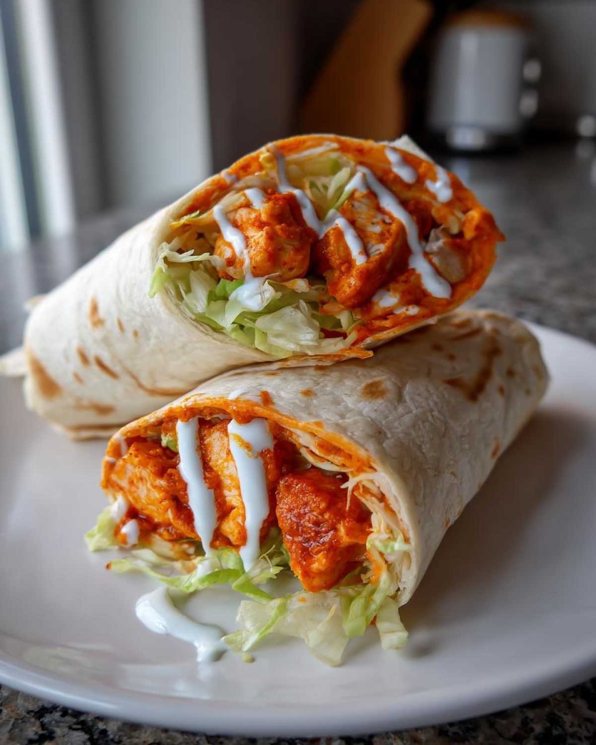 Cross-section of a buffalo chicken wrap filled with orange-sauced chicken, lettuce, and drizzled with ranch dressing.