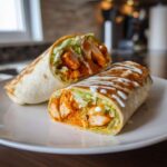 Cross-section of a buffalo chicken wrap showing spicy chicken, lettuce, and a ranch drizzle.