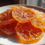 A pile of glistening, bright orange candied orange slices coated in sparkling sugar crystals.
