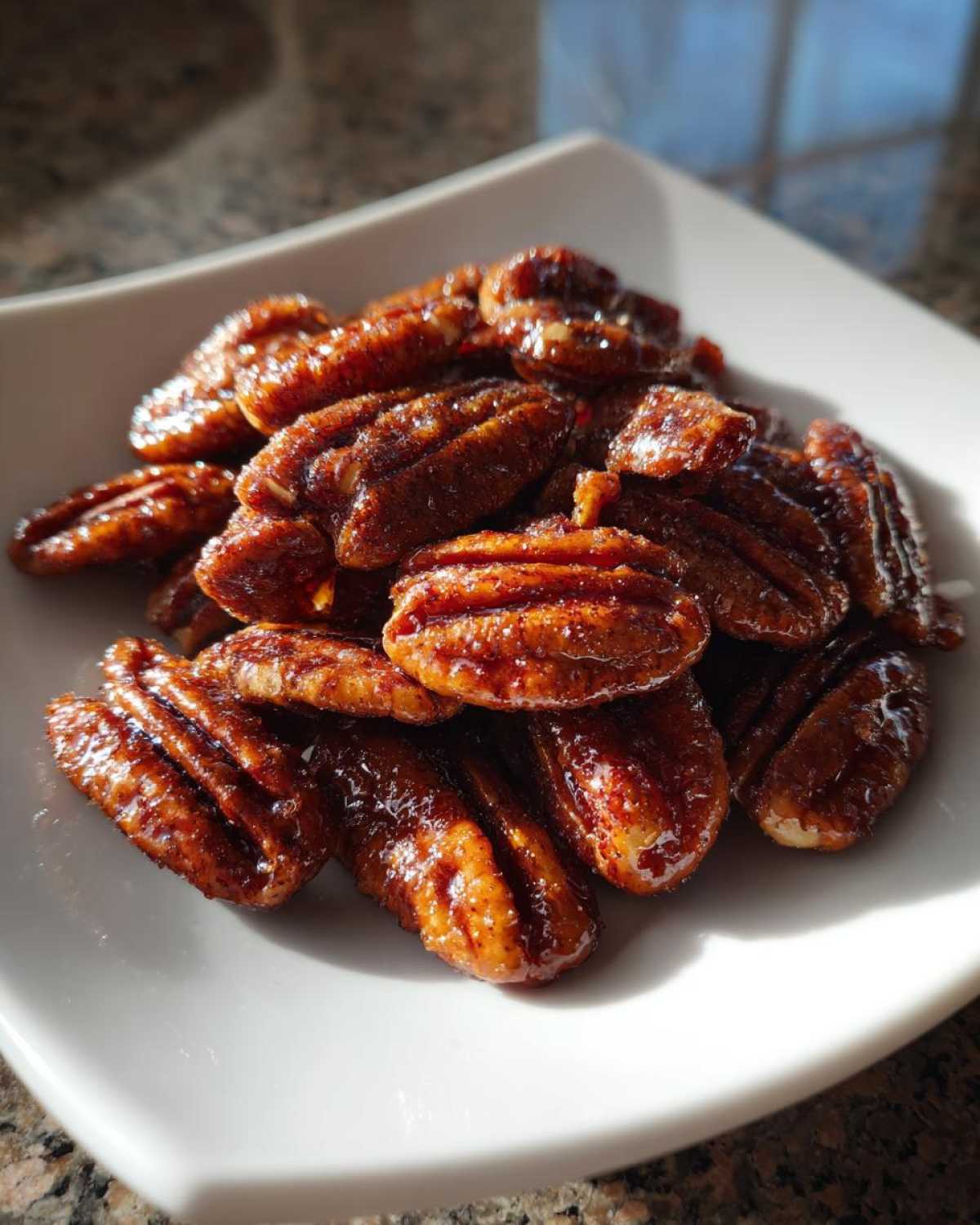 A close-up shot of shiny, caramelized candied pecans piled on a small white dish.