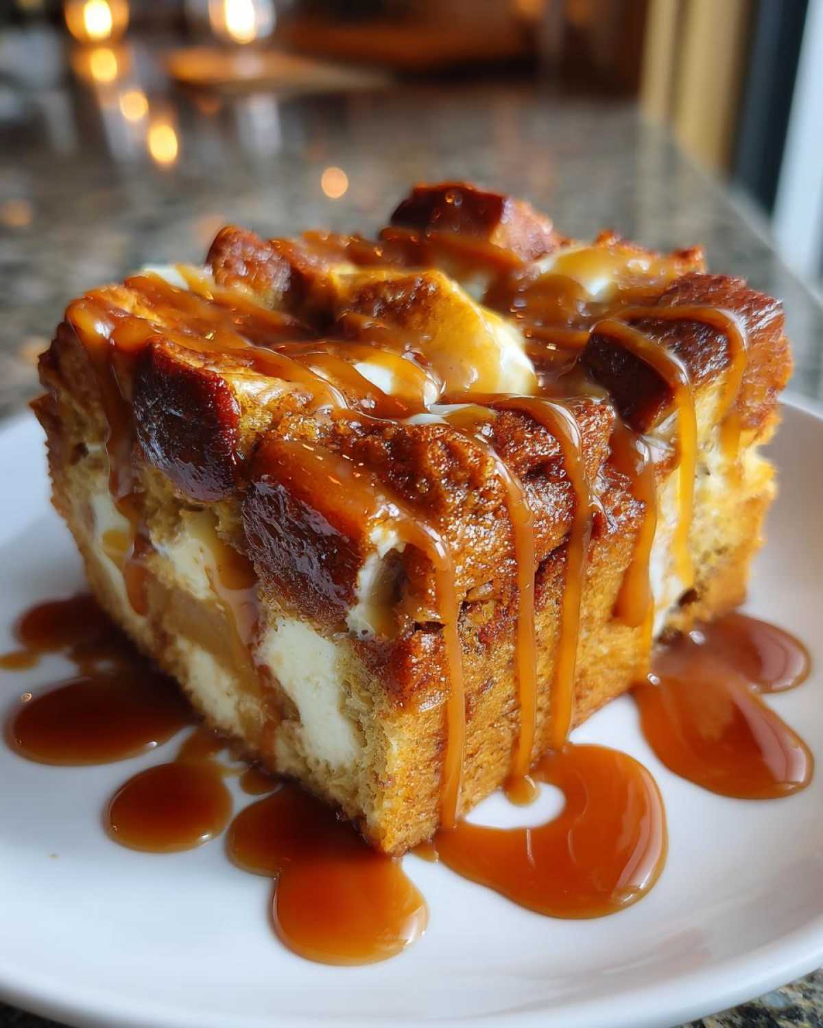 A close-up of a rich slice of apple bread pudding drizzled heavily with caramel sauce.
