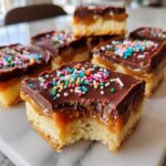 Close-up of caramel ritz cracker christmas cookies bars topped with chocolate and colorful sprinkles, one piece has a bite taken out.