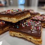 Close-up of stacked caramel ritz cracker christmas cookies topped with chocolate and colorful sprinkles.