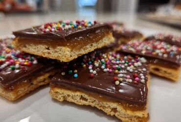 Close-up of stacked caramel ritz cracker christmas cookies topped with chocolate and colorful sprinkles.