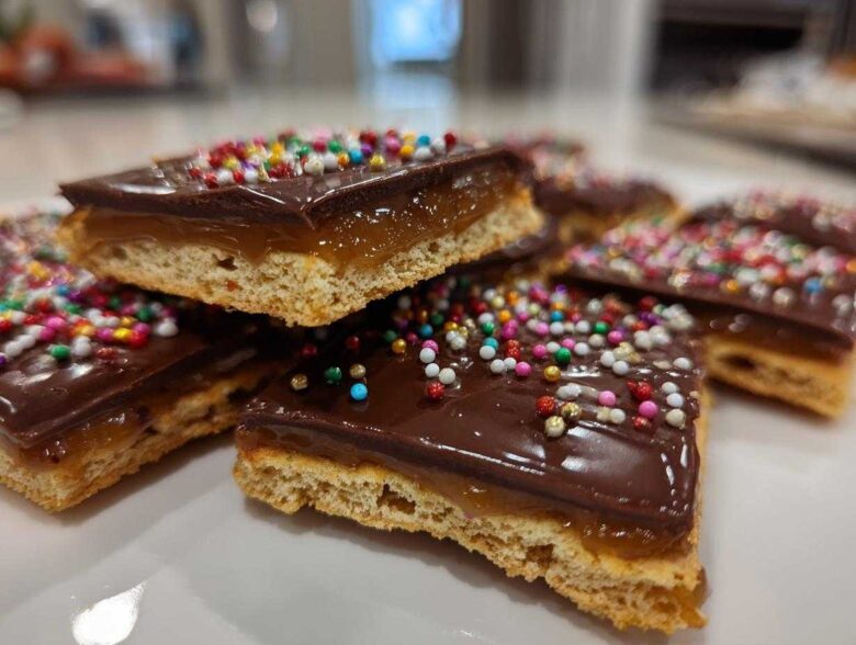 Close-up of stacked caramel ritz cracker christmas cookies topped with chocolate and colorful sprinkles.