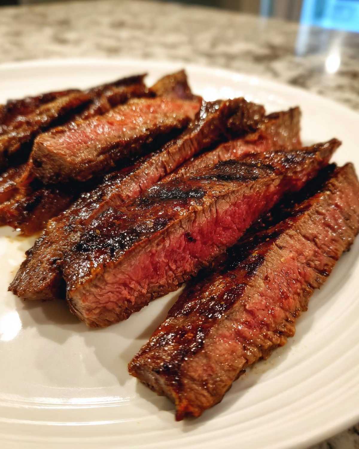 Close-up of medium-rare, sliced steak cooked with carne asada marinade on a white plate.