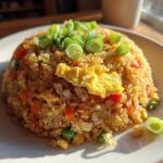A beautifully plated mound of cauliflower fried rice mixed with scrambled egg, carrots, and peas, topped with fresh green onions.