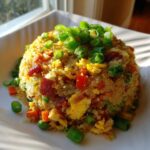 A perfectly molded serving of cauliflower fried rice topped with bright green scallions, showcasing eggs and vegetables.