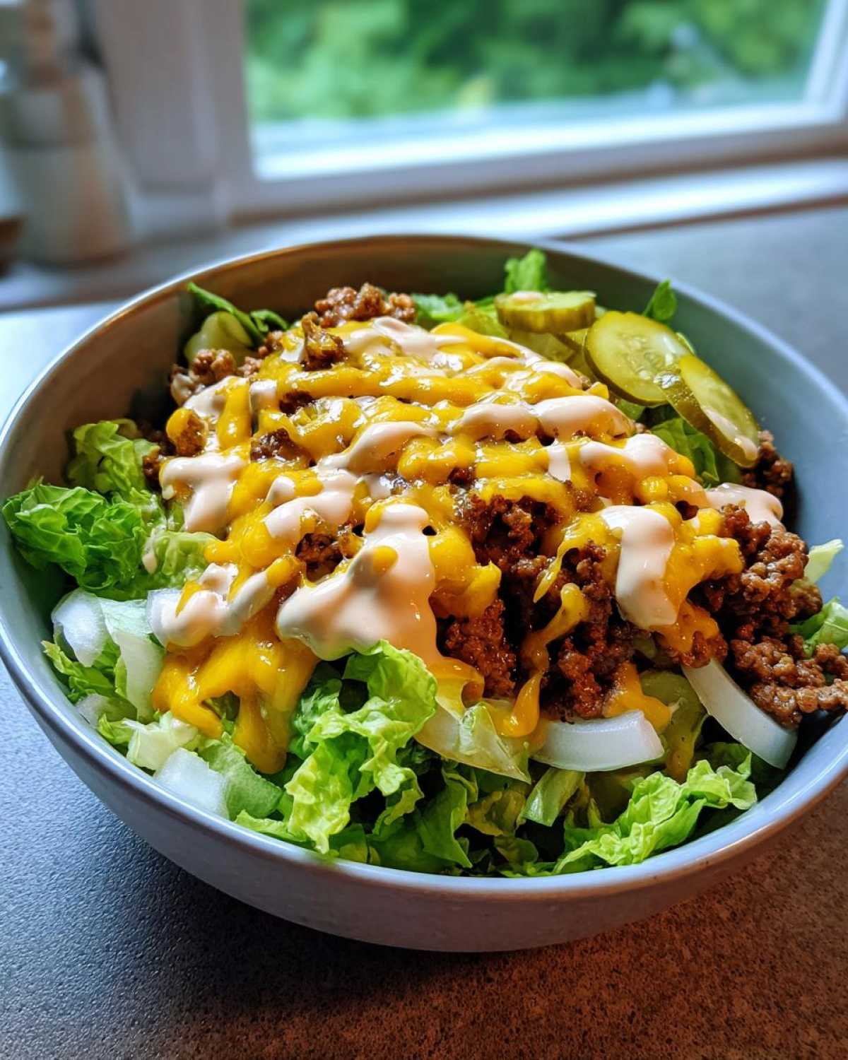 A close-up of a fresh cheeseburger bowl featuring lettuce, seasoned ground beef, melted cheese, and special sauce.