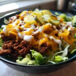 A close-up of a delicious cheeseburger bowl featuring seasoned ground beef, melted cheddar cheese, and a drizzle of white sauce over lettuce.