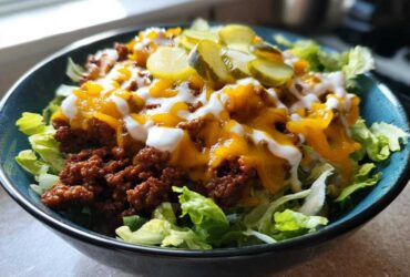 A close-up of a delicious cheeseburger bowl featuring seasoned ground beef, melted cheddar cheese, and a drizzle of white sauce over lettuce.