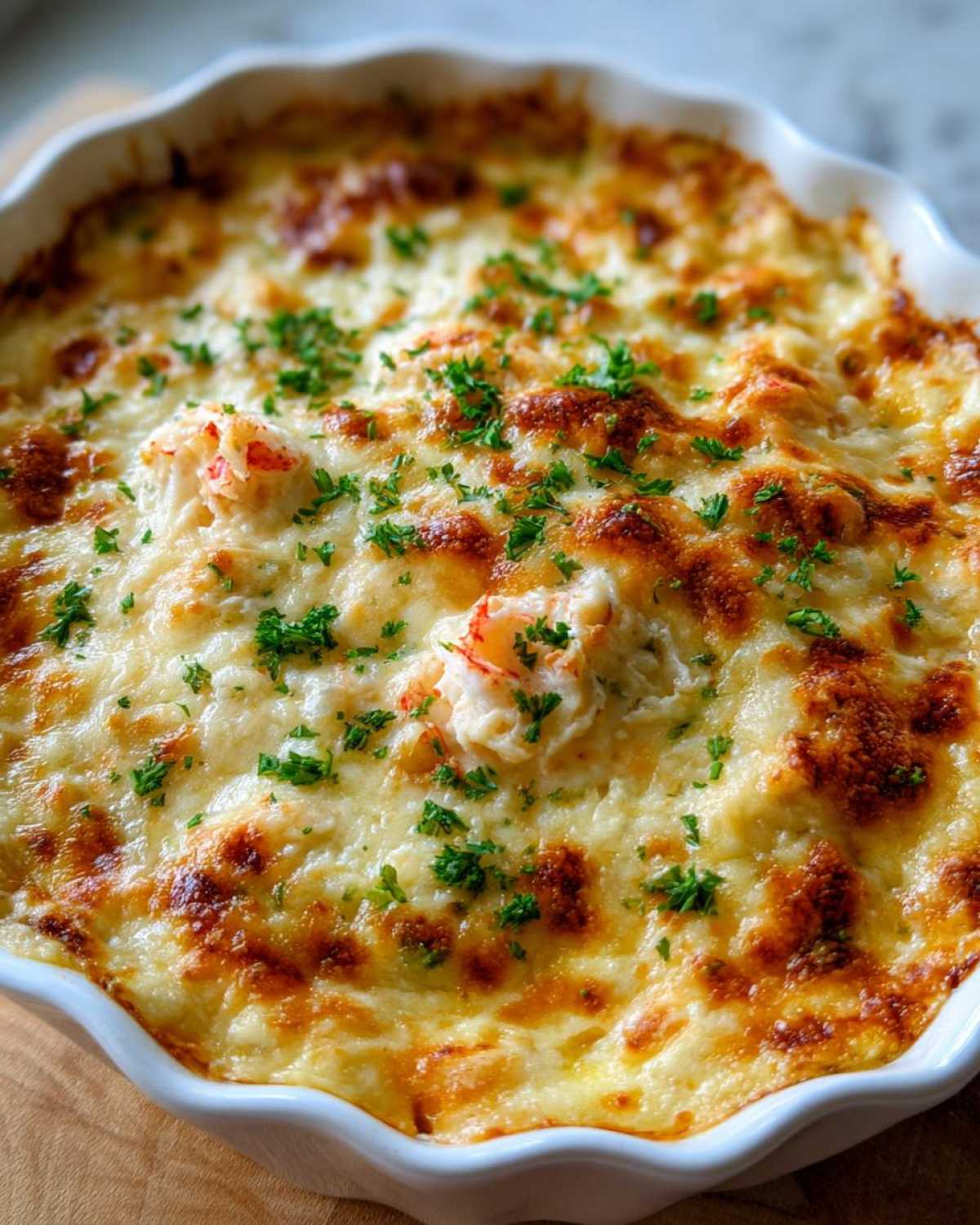 Close-up of a bubbly, baked hot crab dip topped with melted, browned cheese and fresh parsley.