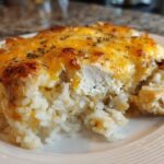 A serving of cheesy chicken and rice casserole showing melted, browned cheese topping over creamy rice and white chicken pieces.