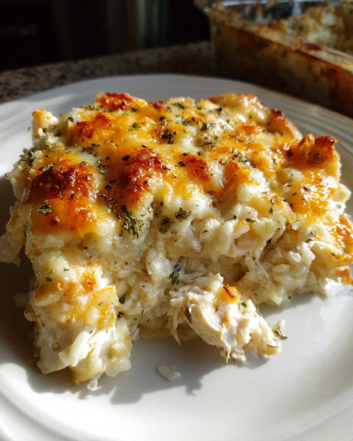 A close-up serving of cheesy chicken and rice casserole with a golden, bubbly cheese topping.
