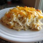 A close-up serving of baked cheesy chicken and rice, topped with melted cheddar cheese.
