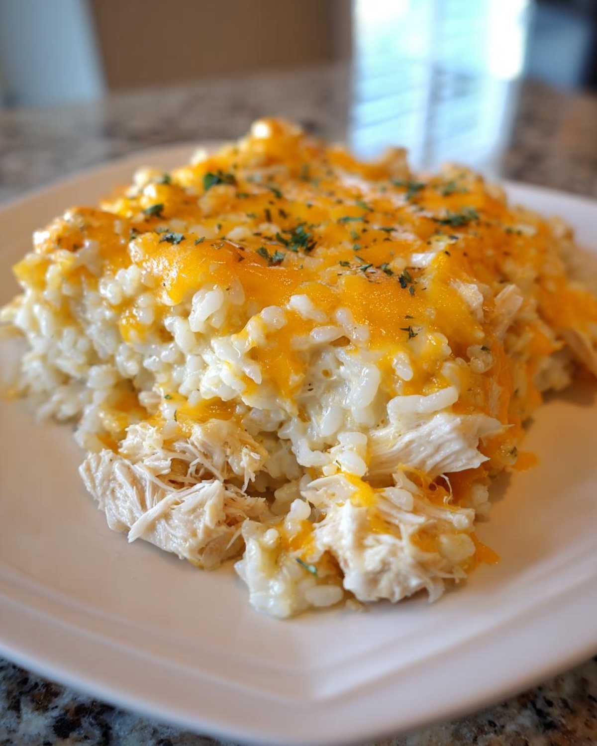 A close-up of a serving of cheesy chicken and rice topped with melted orange cheddar cheese and parsley.