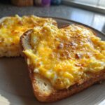 Two slices of golden brown toast topped with fluffy scrambled egg and melted cheddar cheese, making delicious egg toast.