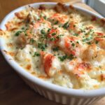 Close-up of a bubbling, cheesy hot crab dip topped with large pieces of white and red crab meat and fresh parsley.