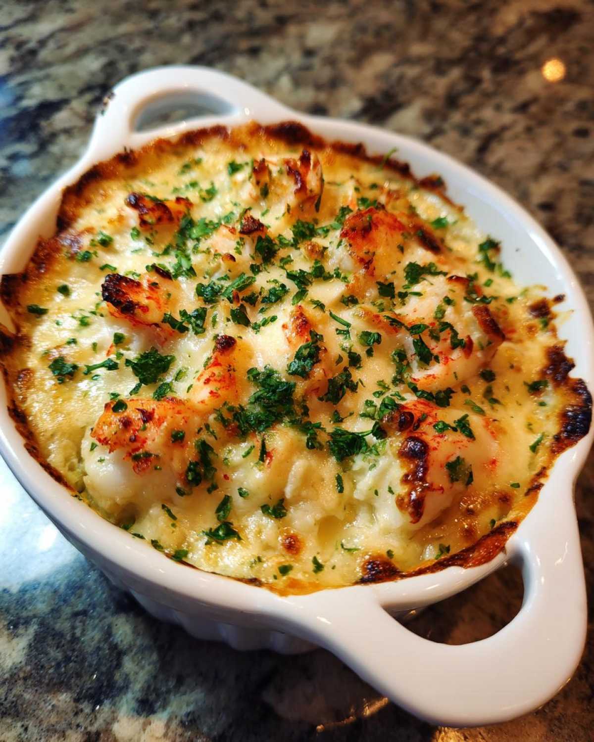 Close-up of creamy, baked hot crab dip topped with chunks of crab and fresh parsley in a white dish.