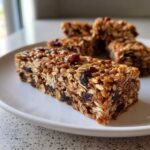 A close-up of a thick, chewy no bake granola bar packed with oats and dried cranberries on a white plate.